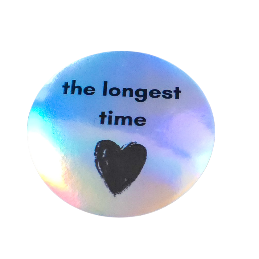 A round holographic sticker with the text 'the longest time' in black lowercase font and a black heart in the center, shown on a plain white background.